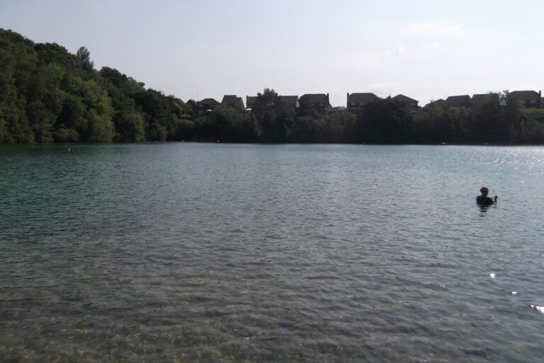 Divers Cove, Godstone: clear turquoise water with a swimmer and houses on the ridge