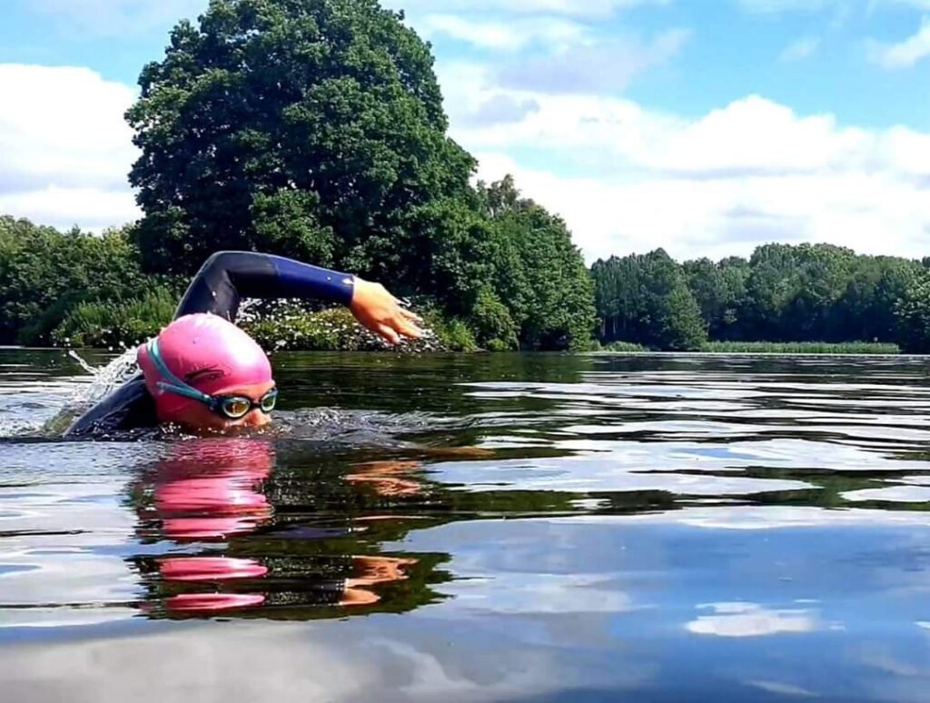 Open water swimmer with a tow float at Alderford Lake, Shropshire, where bell tents and camping pitches are on the lakeshore